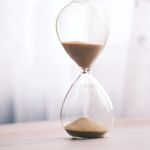 Minimalist hourglass filled with sand symbolizing time and patience, against a soft background.