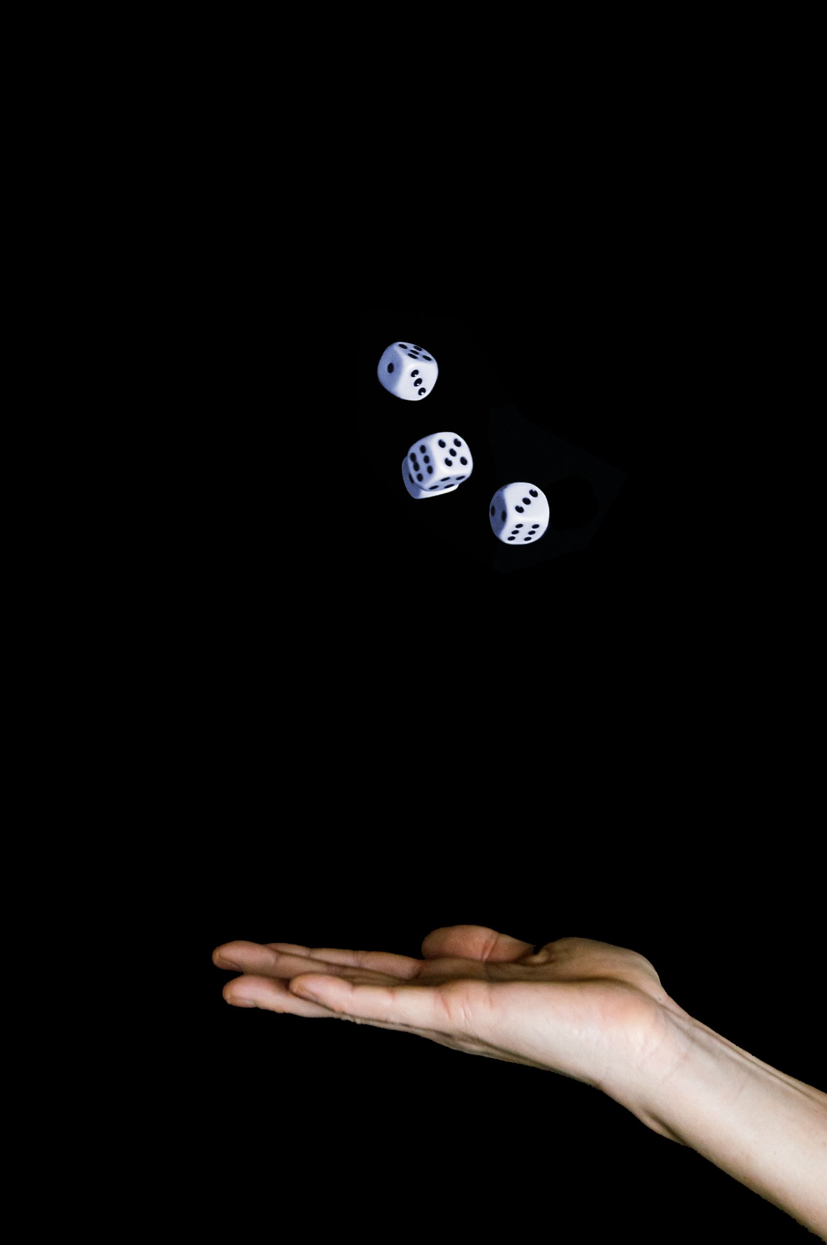 A close-up of three dice floating above an open hand set against a black background.