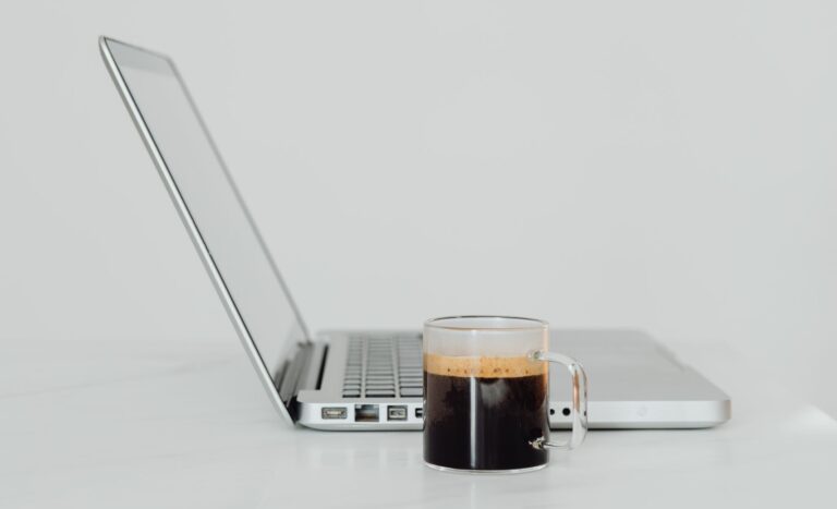 A minimalist setup featuring a laptop and black coffee on a white table, perfect for a productive work environment.