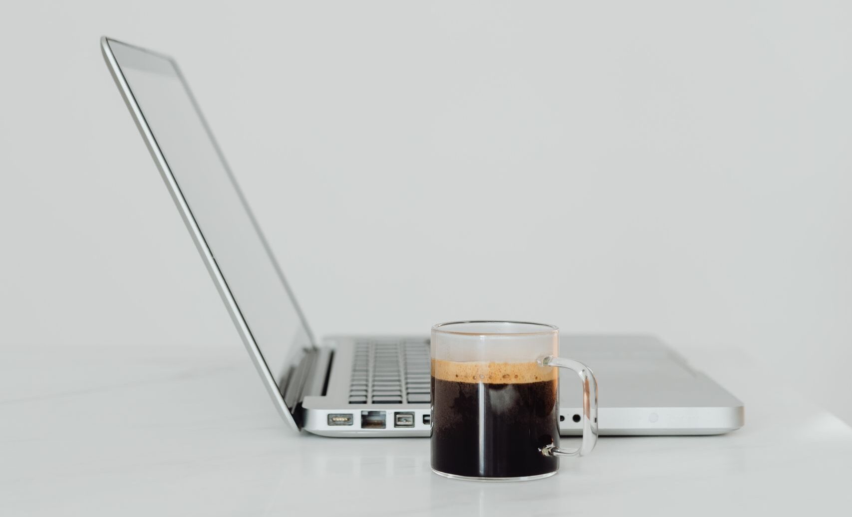 A minimalist setup featuring a laptop and black coffee on a white table, perfect for a productive work environment.