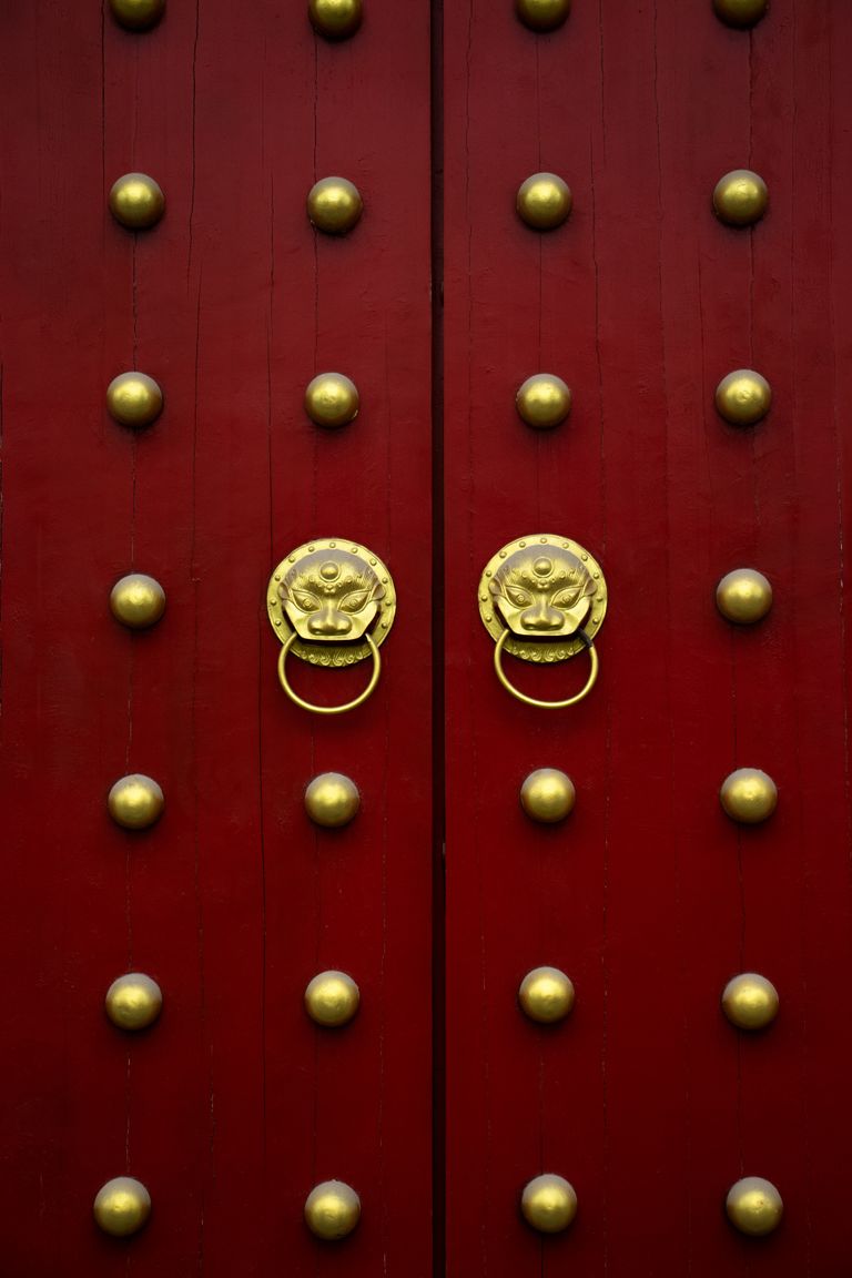 Close-up of a red door with golden lion head knockers, symbolizing traditional architecture.