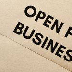 Close-up of an 'Open for Business' sign on a textured brown paper background.