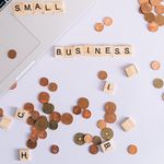 Flat lay of coins, Scrabble tiles spelling 'small business', and laptop, perfect for finance or entrepreneurship themes.