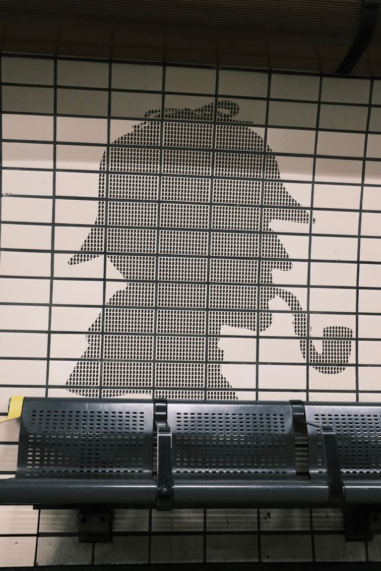 Silhouette of a detective with a pipe on a tiled subway wall.