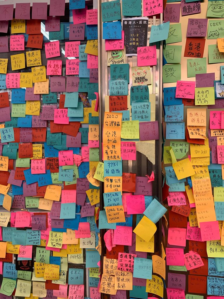 Vibrant wall covered in sticky notes with various messages and colors indoors.