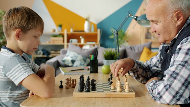 A grandfather and grandson engaged in a thoughtful game of chess in a cozy living room setting.