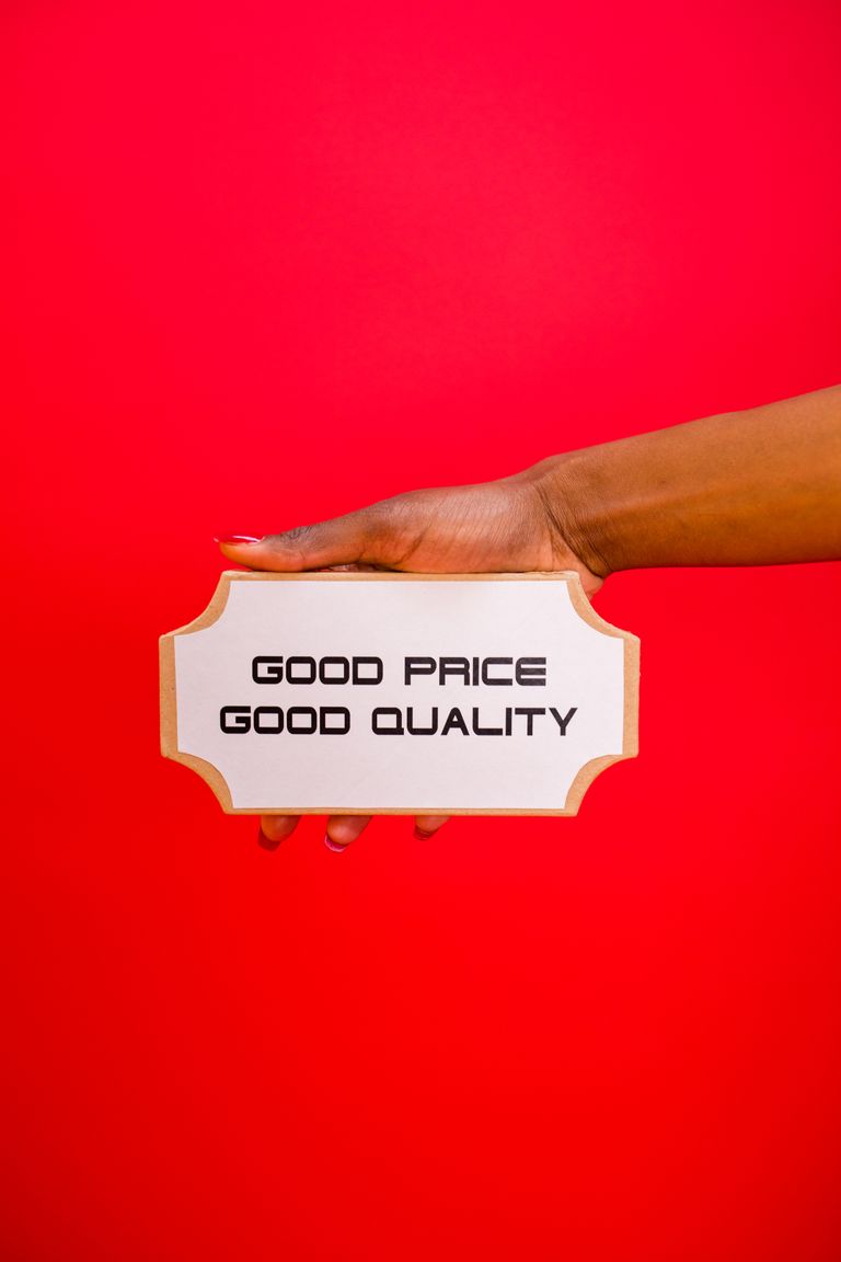 A hand holding a sign with 'Good Price, Good Quality' text against a bright red background.