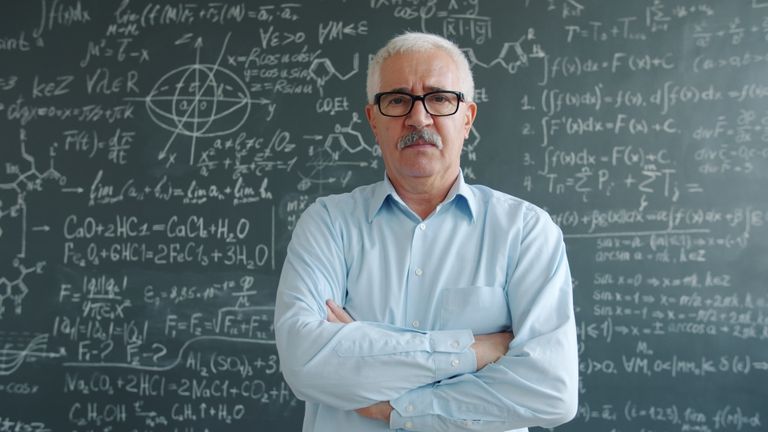 Scientist standing confidently with arms crossed before a chalkboard filled with complex equations.