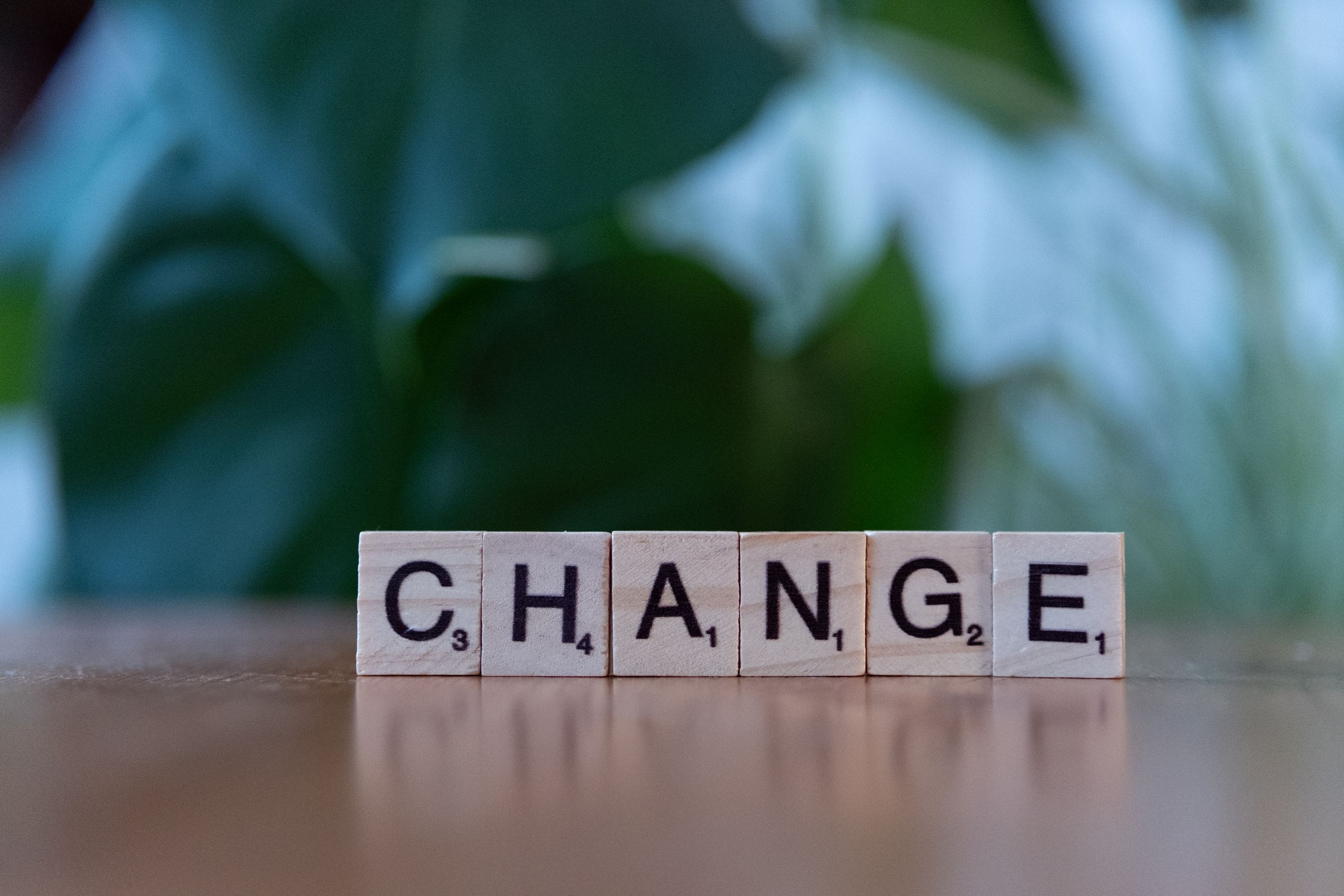 Scrabble tiles spelling 'CHANGE' on a wooden surface with a blurred green background.