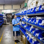 A worker in a warehouse organizing inventory on shelves with blue bins.