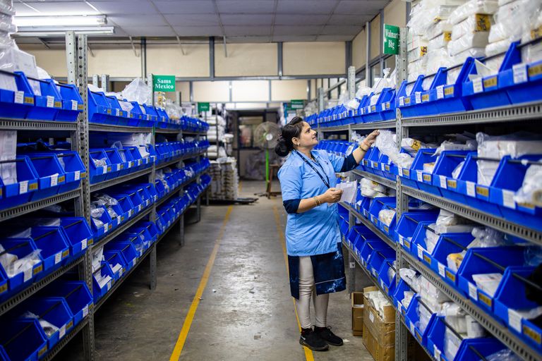 A worker in a warehouse organizing inventory on shelves with blue bins.